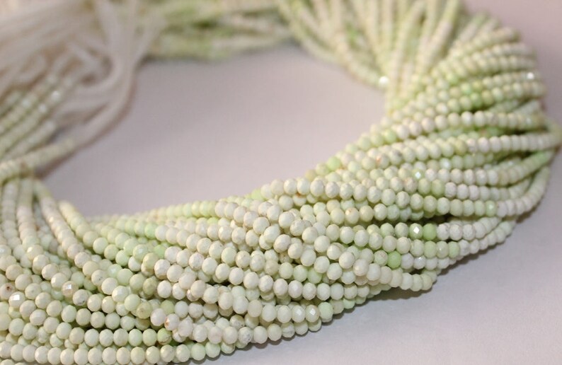 May include: Close-up of a collection of light green, faceted beads. The beads are strung together, forming multiple strands. The beads have a subtle sheen and are arranged in a circular pattern, suggesting they are ready for jewelry making.