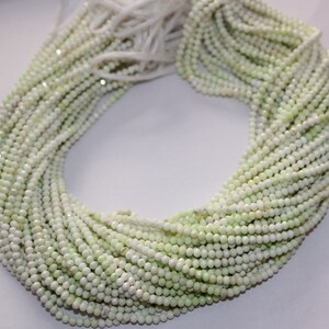 May include: A collection of light green and white round beads, strung together in multiple strands. The beads have a slightly faceted appearance, creating a subtle sparkle. The strands are bundled together, with a few loose strands visible at the top.