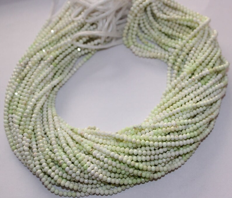 May include: A collection of light green and white round beads, strung together in multiple strands. The beads have a slightly faceted appearance, creating a subtle sparkle. The strands are bundled together, with a few loose strands visible at the top.