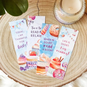 K&ouml;nnte beinhalten: Vier farbenfrohe Lesezeichen mit Aquarell-Illustrationen von Cupcakes, Donuts und anderen s&uuml;&szlig;en Leckereien. Die Lesezeichen zeigen inspirierende Zitate &uuml;ber das Lesen, wie "Heute bin ich dankbar f&uuml;r B&uuml;cher!" und "Im Zweifel, lies ein Buch!"
