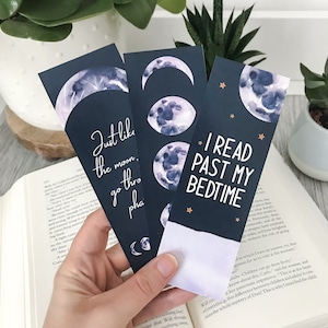 May include: Three rectangular bookmarks with a dark blue background featuring watercolor moon phases and stars. One bookmark displays the text "Just like the moon, we go through phases," while another features the text "I READ PAST MY BEDTIME."