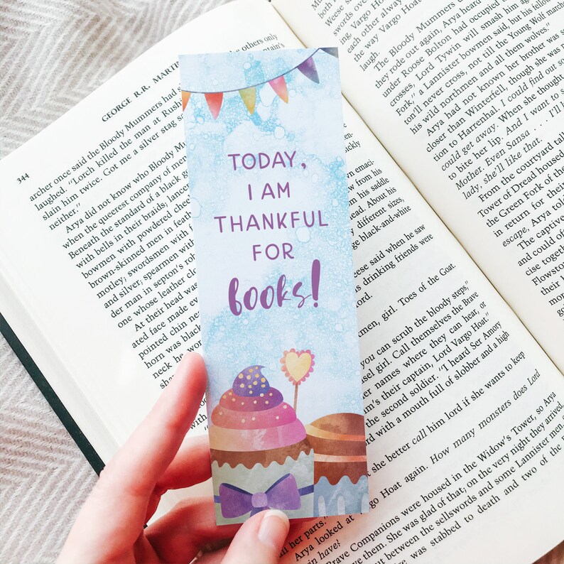 K&ouml;nnte beinhalten: Ein blaues und wei&szlig;es Lesezeichen mit einem Cupcake-Design. Das Lesezeichen tr&auml;gt den Text "Heute bin ich dankbar f&uuml;r B&uuml;cher!"