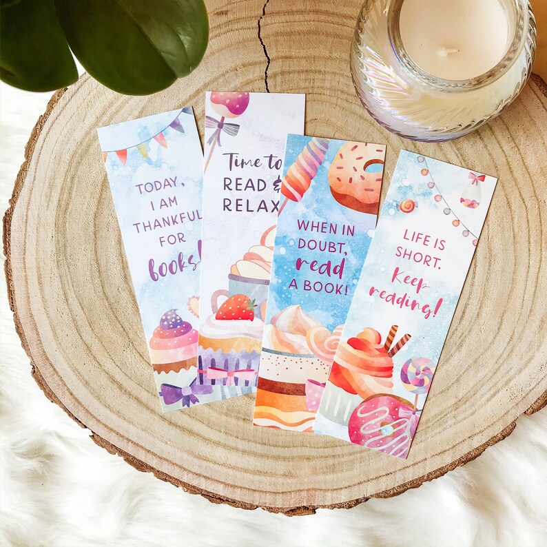 K&ouml;nnte beinhalten: Vier farbenfrohe Lesezeichen mit Aquarell-Illustrationen von Cupcakes, Donuts und anderen s&uuml;&szlig;en Leckereien. Die Lesezeichen zeigen inspirierende Zitate &uuml;ber das Lesen, wie "Heute bin ich dankbar f&uuml;r B&uuml;cher!" und "Im Zweifel, lies ein Buch!"