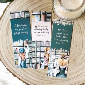May include: Three bookmarks with watercolor illustrations of women in a library. The bookmarks have quotes about adventure, collecting books, and finding yourself in books. The quotes are: "Adventure is just a page away", "When we are collecting books, we are collecting happiness", and "We lose ourselves in books. We find ourselves there too."