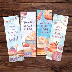 K&ouml;nnte beinhalten: Vier farbenfrohe Lesezeichen mit Aquarell-Illustrationen von Cupcakes, Donuts und anderen s&uuml;&szlig;en Leckereien. Jedes Lesezeichen zeigt ein anderes inspirierendes Zitat &uuml;ber das Lesen. Die Zitate lauten: "Heute bin ich dankbar f&uuml;r B&uuml;cher!" "Zeit zum Lesen und Entspannen" "Im Zweifel, lies ein Buch!" "Das Leben ist kurz. Lies weiter!"