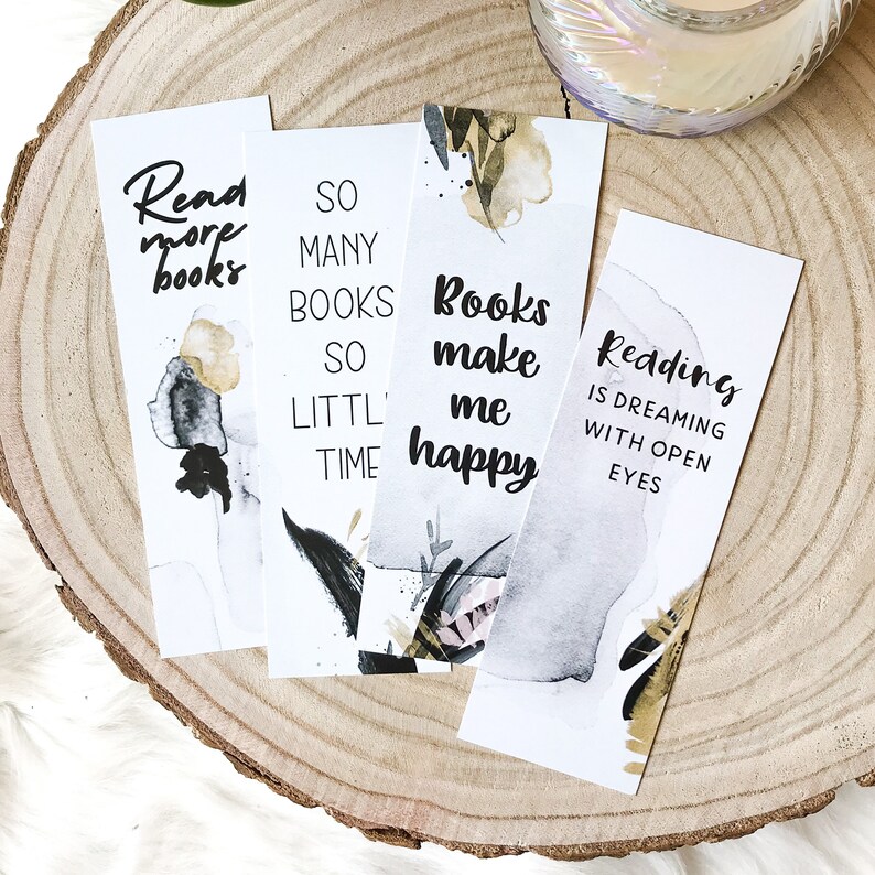 May include: Four white bookmarks with black and gold watercolor designs and inspirational quotes about reading. The quotes are "Read more books", "So many books so little time", "Books make me happy", and "Reading is dreaming with open eyes".