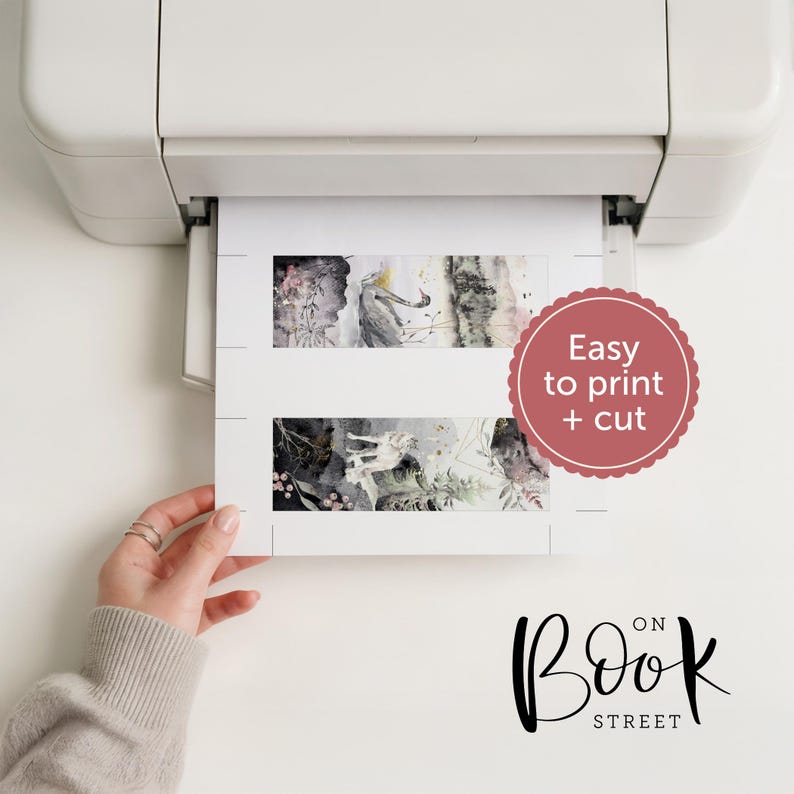May include: A white printer outputting a sheet of paper with two rectangular bookmarks featuring watercolor illustrations of a wolf and forest elements. A pink scalloped circle contains the text Easy to print + cut. The logo Book on Street is visible.