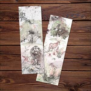 May include: Two rectangular paper bookmarks featuring watercolor illustrations. One bookmark displays a brown bear amidst muted green trees and floral accents. The second bookmark depicts a deer with antlers, surrounded by trees and soft floral elements.