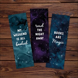 May include: Three galaxy-themed bookmarks with inspirational quotes. The first bookmark is teal blue with white stars and the text "My weekend is all booked". The second bookmark is purple with white stars and the text "Read the night away". The third bookmark is dark blue with white stars and the text "Books are magic".