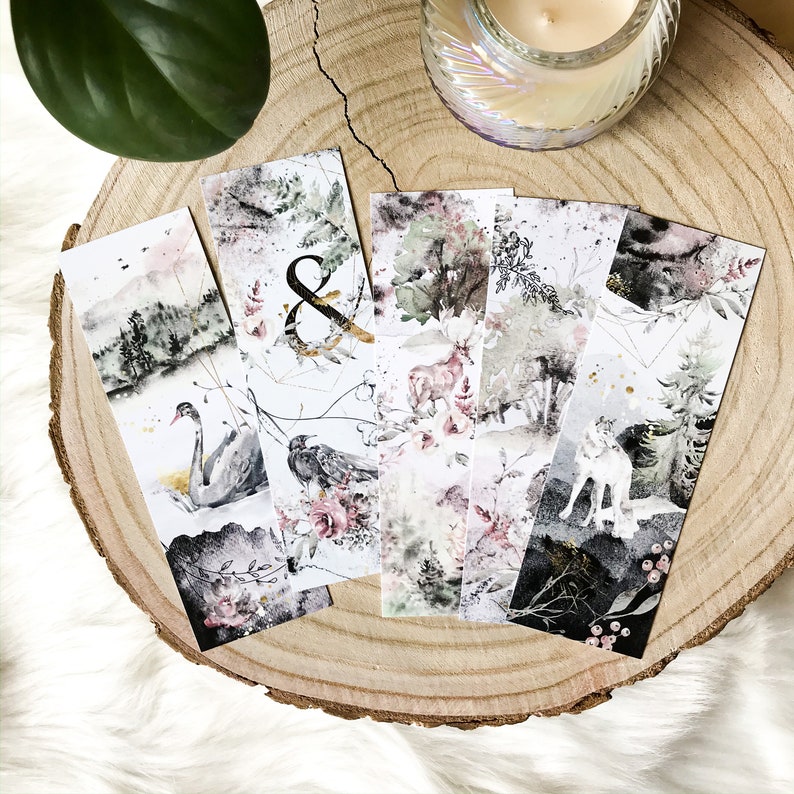 May include: Five rectangular paper bookmarks featuring watercolor illustrations. Designs include a swan on water, an ampersand symbol, a deer in a forest, floral patterns, and a wolf in a dark woodland setting with black, white, green, and pink tones.