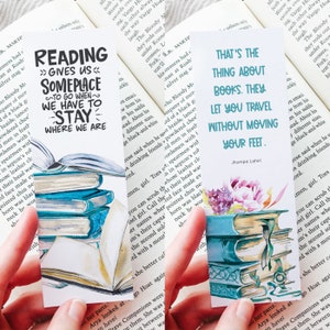 May include: Three colorful bookmarks with watercolor illustrations of stacked books and floral designs. The bookmarks feature inspirational quotes about reading and travel. The first bookmark reads "Reading gives us someplace to go when we have to stay - where we are". The second bookmark reads "That's the thing about books. They let you travel without moving your feet." The third bookmark reads "That's the thing about books. They let you travel without moving your feet."