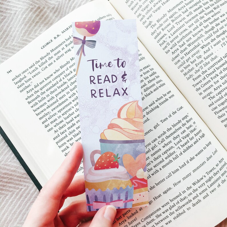 K&ouml;nnte beinhalten: Ein farbenfrohes Lesezeichen mit einem verspielten Design mit Cupcakes und Erdbeeren. Das Lesezeichen tr&auml;gt den Text "Time to Read & Relax" in schwarzer Schrift.