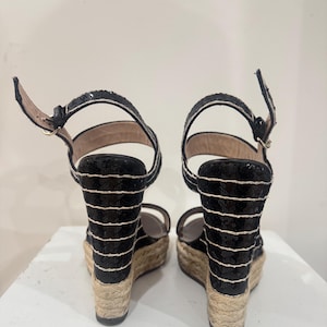 May include: Pair of black sequined wedge sandals with white horizontal stripes. The sandals have ankle straps and woven jute soles. The heels are approximately 4 inches high.