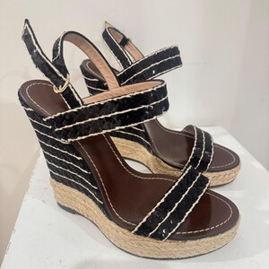 May include: Pair of black sequin wedge sandals with white trim and brown insoles. The wedge heels have a woven texture. The sandals have adjustable ankle straps and a classic design.