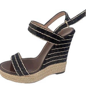 May include: Black wedge sandals with a woven jute sole and black fabric straps. The straps are accented with white trim. The wedge heel is approximately 4 inches high.