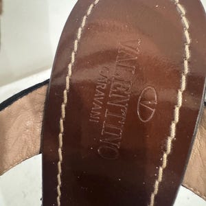 May include: Close-up of a brown leather sandal sole with the brand name "VALENTINO GARAVANI" embossed. The sole is stitched with a light-colored thread.