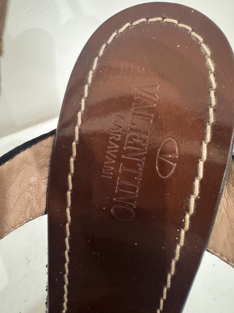 May include: Close-up of a brown leather sandal sole with the brand name "VALENTINO GARAVANI" embossed. The sole is stitched with a light-colored thread.