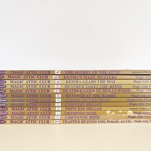 May include: A stack of eleven Magic Attic Club books with tan spines and purple text. Titles include The Secret of the Attic, Keisha's Maze Mystery, Keisha Leads the Way, Heather Takes the Reins, Heather Goes to Hollywood, Heather at the Barre, Alison on the Trail, Cowgirl Megan, Princess Megan, Champion Rose, Cheyenne Rose, and Trapped Beyond the Magic Attic.