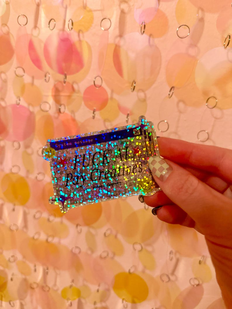 May include: A rectangular holographic sticker with a glittery finish featuring a dark blue computer window design. The text reads System message, FUCK AI, Pay Creatives, and @doodlymeg, accented with small red stars and yellow smiley faces.