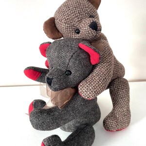 May include: Two brown tweed teddy bears with red accents. The smaller bear is sitting and the larger bear is standing on top of the smaller bear.