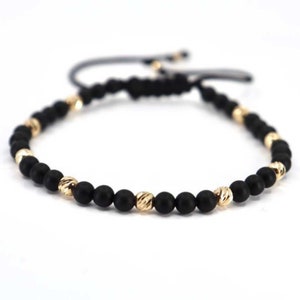 Op de afbeelding: Een zwarte en gouden kralen armband met een zwarte koordsluiting. De armband heeft afwisselend zwarte en gouden kralen.