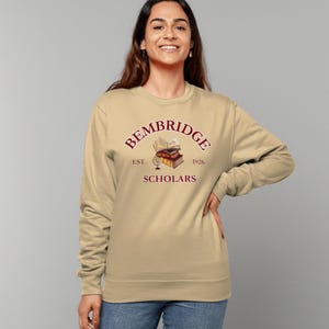May include: A beige sweatshirt with a maroon graphic of a stack of books, a globe, and the text "Bembridge Scholars Est. 1926".