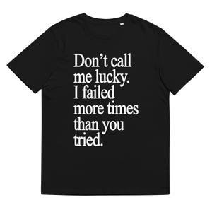 May include: Black t-shirt with white text that reads "Don't call me lucky. I failed more times than you tried."
