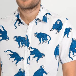 May include: A white button-down shirt with a blue monkey print. The shirt has short sleeves and a collared neckline.
