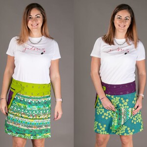 May include: Two women wearing white t-shirts with different lipstick designs. Both women are wearing colourful wrap skirts with a green and purple belt. The skirts have pockets and are made of different fabrics.