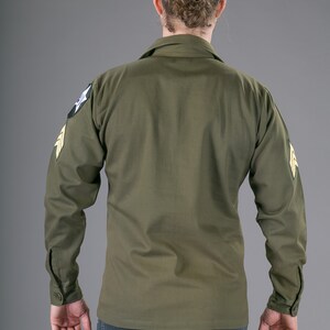 May include: A green long-sleeved shirt with a patch on the left shoulder and another on the right sleeve. The patches are yellow and green with a star and a wing design.