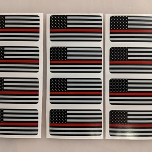 以下が含まれることがあります： アメリカの国旗のデザインが施された長方形のステッカーが9枚。各ステッカーには、白黒のアメリカ国旗に中央に赤いストライプが1本入っています。