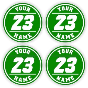 Könnte beinhalten: Vier grüne und weiße runde Aufkleber. Jeder Aufkleber zeigt die weiße Zahl 23, das Wort "YOUR" darüber und "NAME" darunter. Die Aufkleber sind im Sport-Design gestaltet.
