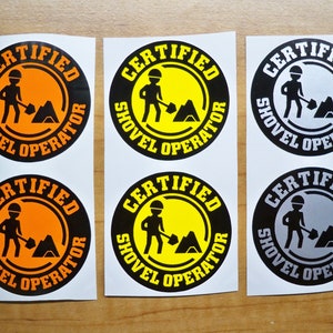 Puede incluir: Seis pegatinas circulares con borde negro. Cada pegatina muestra el texto "CERTIFIED SHOVEL OPERATOR". El gráfico central muestra una persona con una pala. Los colores de fondo varían entre naranja, amarillo y gris.