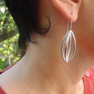May include: Silver dangle earrings with a geometric design. The earrings are made of three overlapping ovals.