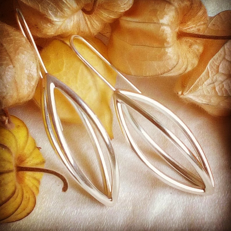 May include: A pair of silver dangle earrings with a delicate, geometric design. The earrings are shaped like elongated leaves with a double-layered, openwork pattern.