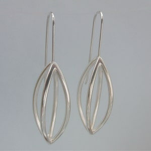 May include: A pair of silver dangle earrings with a geometric leaf design.
