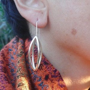 May include: Silver dangle earrings with a double oval design. The earrings are hanging from a person's ear.