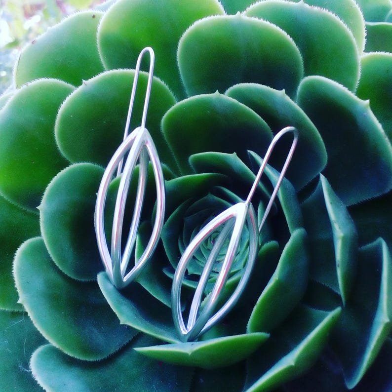 May include: A pair of silver earrings with a leaf design. The earrings are delicate and have a modern look.