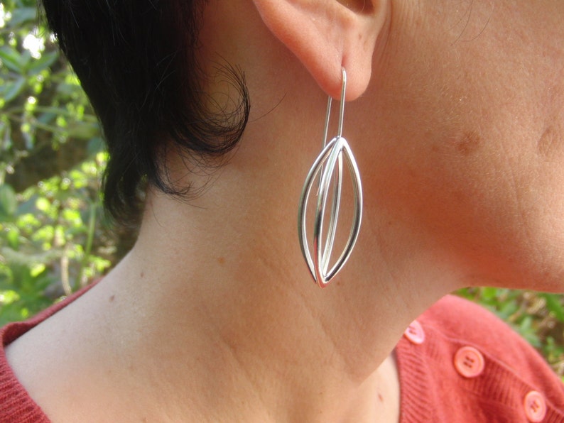 May include: Silver dangle earrings with a geometric design. The earrings are made of three overlapping ovals.