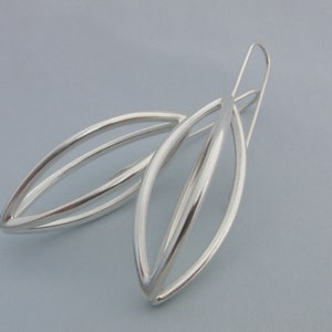 May include: A pair of silver earrings with a simple, modern design. The earrings are made of two overlapping ovals, creating a delicate and elegant look.
