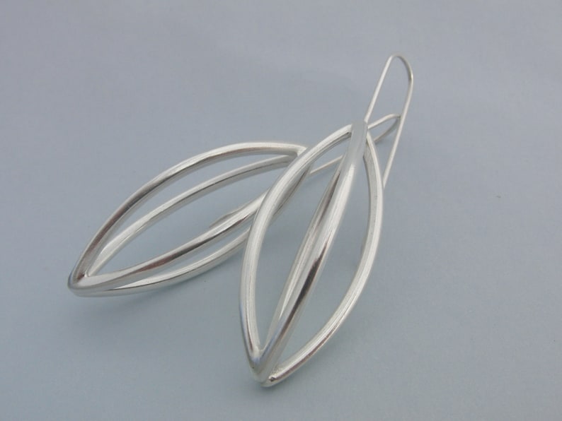 May include: A pair of silver earrings with a simple, modern design. The earrings are made of two overlapping ovals, creating a delicate and elegant look.