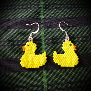 May include: A pair of yellow rubber ducky earrings with silver hooks. The ducks are made of small yellow beads and have orange beaks.