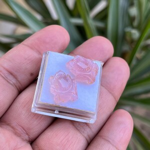 K&ouml;nnte beinhalten: Ein Paar rosa geschnitzte Rosenohrringe in einer kleinen durchsichtigen Plastikbox.