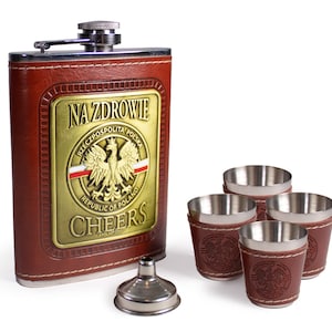 Puede incluir: Una petaca de acero inoxidable cubierta de cuero marrón con un emblema dorado que presenta el escudo de armas polaco y el texto "NA ZDROWIE" y "CHEERS". La petaca viene con cuatro pequeños vasos de chupito de acero inoxidable con cubiertas de cuero marrón y un embudo plateado.