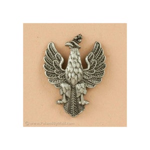 May include: A silver-colored metal eagle emblem with outstretched wings, a crown, and detailed feathering. The emblem is likely a national symbol or heraldic design. The website www.PolandByMail.com is visible at the bottom.