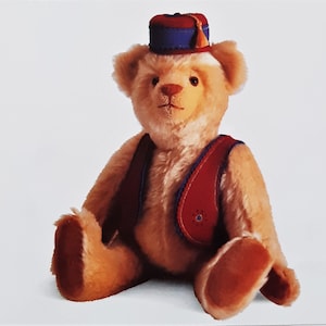 May include: A plush teddy bear wearing a red and blue vest and a red and blue fez hat. The bear is sitting on a white background.