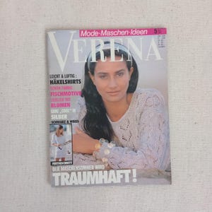 Puede incluir: Un número de la revista Verena titulado Mode-Maschen-Ideen que muestra a una persona con cabello largo y oscuro vistiendo un suéter de punto gris claro. La portada incluye texto como Leicht & Luftig, Häkelshirts, Fischmotive y Traumhaft, junto con una pequeña foto insertada de una persona con un vestido blanco.