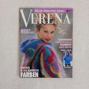 Op de afbeelding: Een uitgave van het vintage tijdschrift Verena uit oktober 1991 met een persoon in een veelkleurige, pluizige gebreide trui met capuchon. De cover bevat de tekst Mode-Maschen-Ideen, Verena, Neu im Herbst en Stricken in den schönsten Farben.