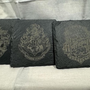 May include: Set of five black slate coasters with the Hogwarts house crests: Gryffindor, Ravenclaw, Hufflepuff, Slytherin, and a Hogwarts crest.