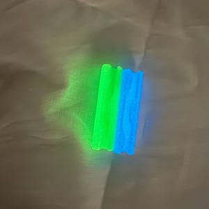 May include: Two glowing, rectangular objects. One is bright green, the other is blue. Both have a textured, wavy design on one side. The objects are on a white surface.